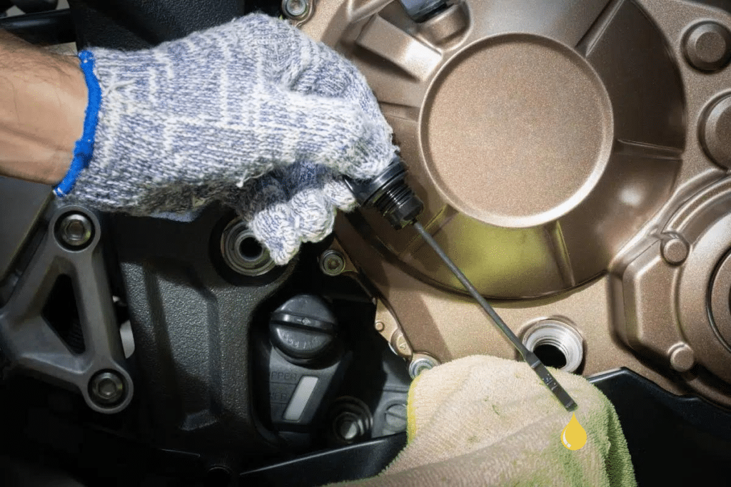 Les 5 astuces pour un entretien moto au top ! Main gantée d'un mécanicien vérifiant le niveau d'huile d'un moteur de moto à l'aide d'une jauge, avec un chiffon vert à proximité pour éviter les déversements d'huile