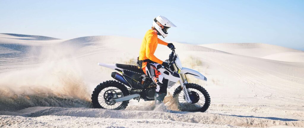 Sport extrême, moto et athlète avec du sable sur roues, de la fierté, de l'habileté et de l'adrénaline. B