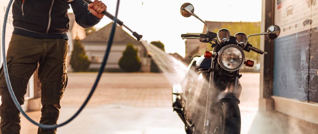 Homme nettoyant une moto avec un jet d'eau à haute pression.