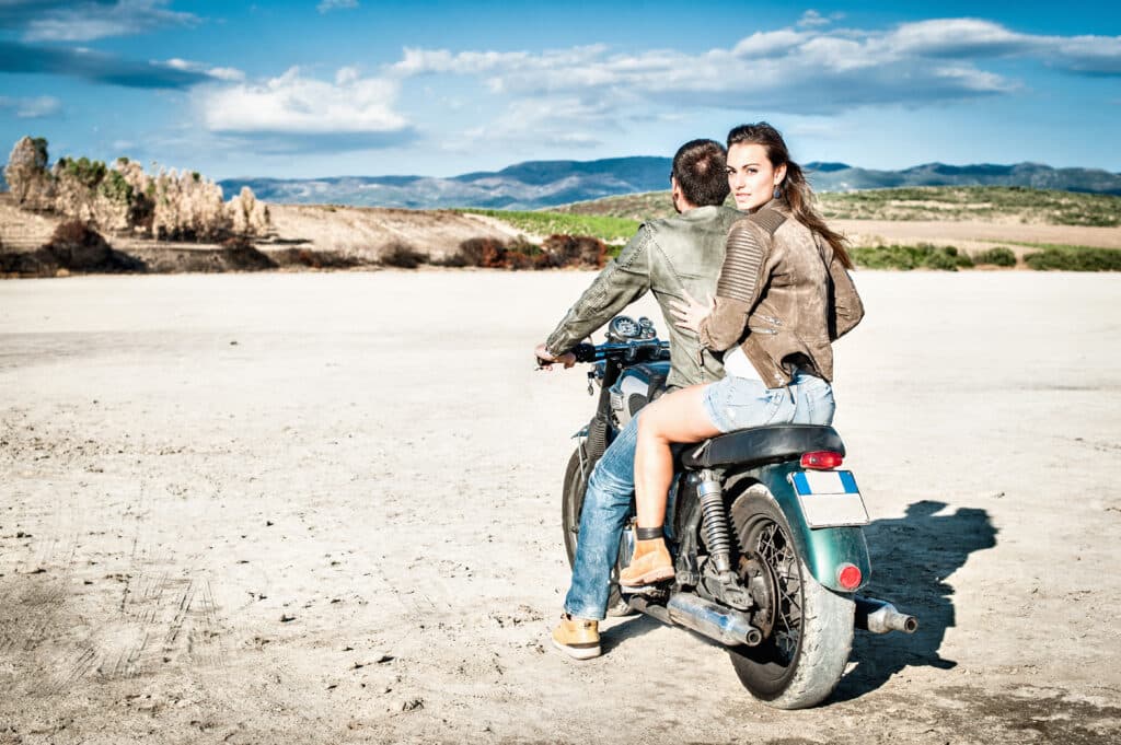 Rear view of young couple riding motorcycle on arid plain, Cagliari, Sardinia, Italy