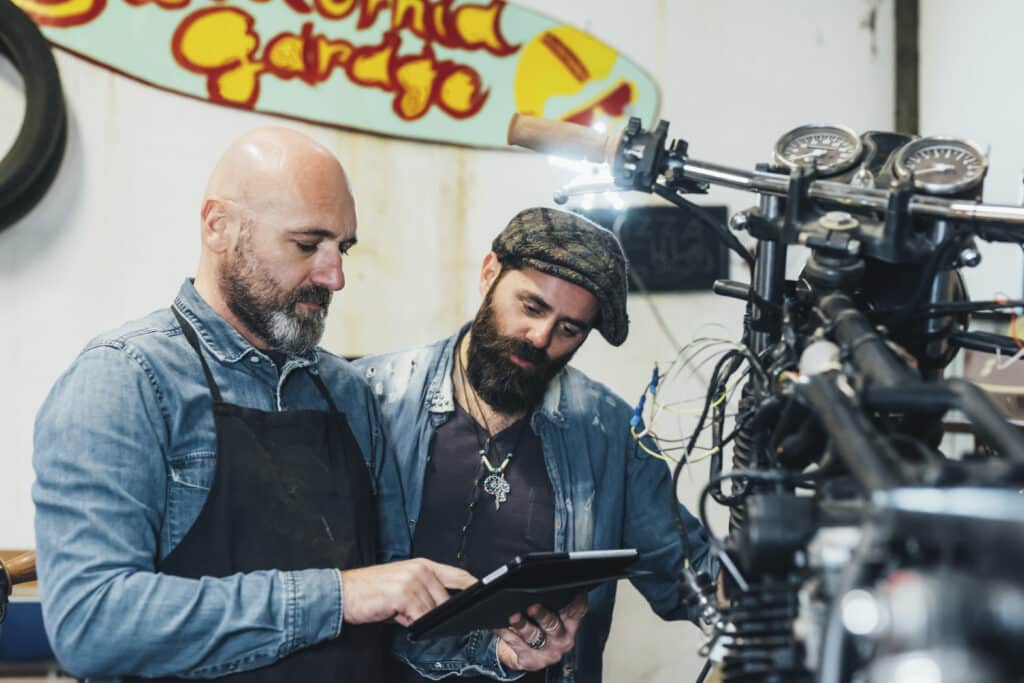 Two mature men, working in garage, using digital tablet