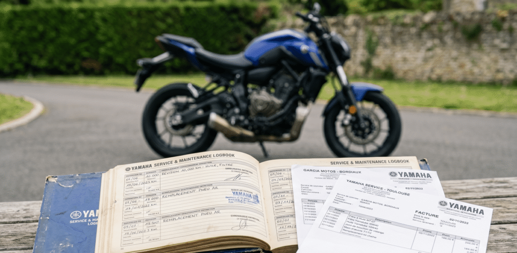 gros plan sur un carnet d'entretien ouvert avec factures posées dessus, en parallèle avec une moto propre en arrière-plan
