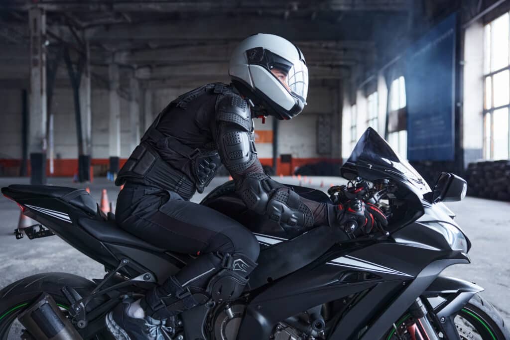 Biker wearing protective helmet and uniform for speed riding at training class of motordrome of professional driving school