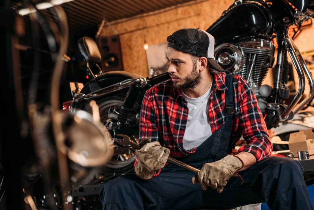 handsome bike repair station worker with wrench sitting in front of motorcycle