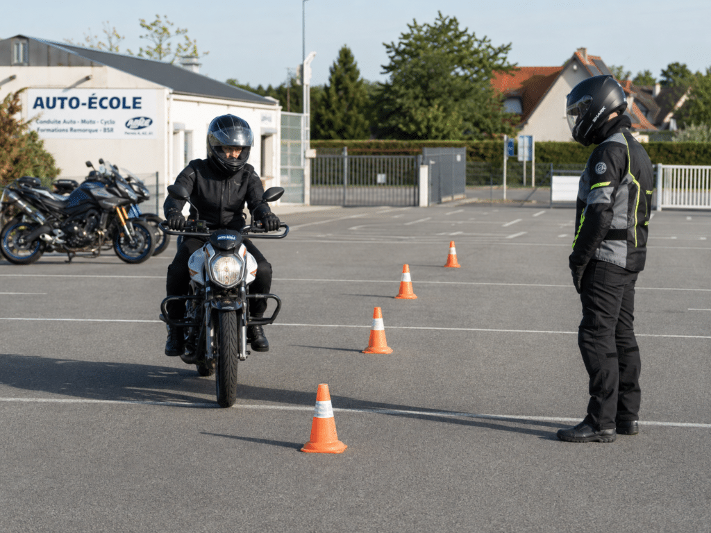 photorealistic, motorcycle training school plateau exercise, student rider on a small motorcycle performing slow-speed slalom between orange cones, instructor watching from the side, safety gear worn by both, bright morning light, suburban driving school setting, no watermark
