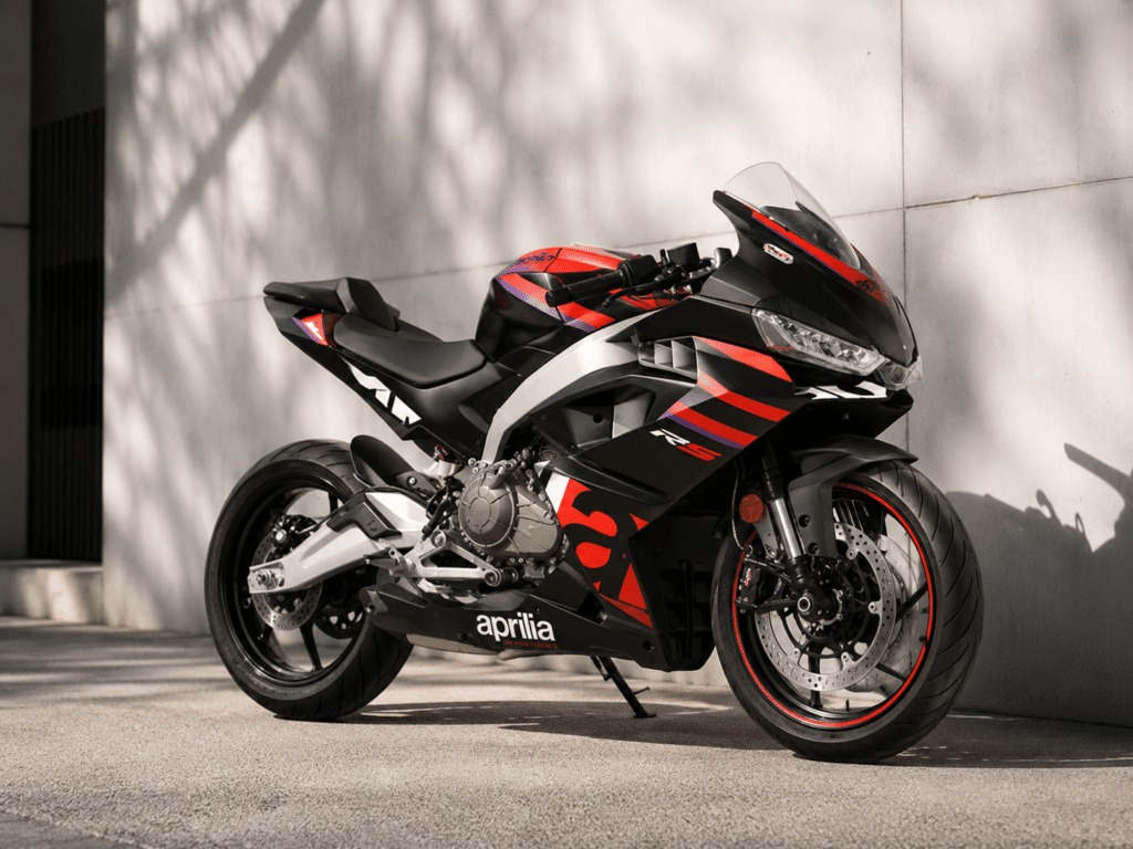photorealistic, Aprilia RS 457 in Aprilia Racing red livery parked against a white wall in an urban setting, aggressive MotoGP-inspired fairing details visible, RS-GP design cues, dramatic low side angle, dramatic side shadows, premium Italian motorcycle atmosphere, no rider, no watermark