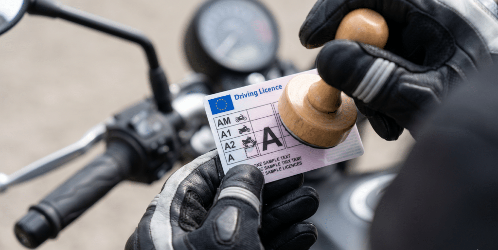 photorealistic, close-up of a motorcycle license with category "A" stamp being added over "A2", held in a hand wearing a motorcycle glove, blurred motorcycle handlebar in background, natural light, shallow depth of field, no watermark