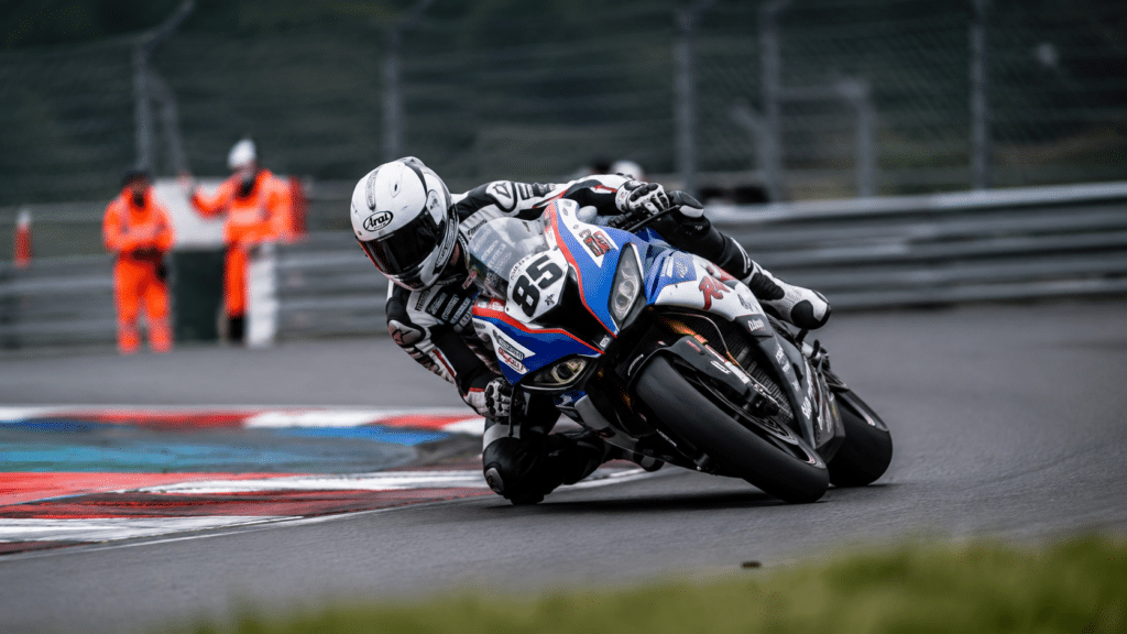 photorealistic race track circuit with a sport motorcycle leaning into a corner at high speed, professional track day atmosphere with safety barriers and marshals visible, dynamic action shot, controlled and legal high speed environment, no rider face identifiable, no watermark