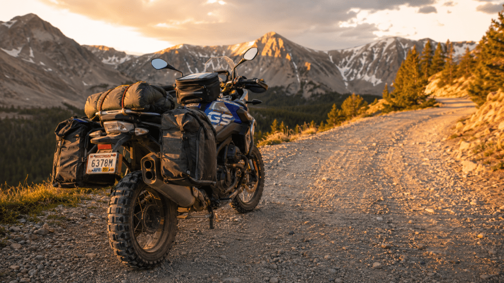 photorealistic adventure motorcycle loaded with soft luggage panniers and tank bag on a gravel mountain road at golden hour, sense of long-distance travel capability, rear three-quarter view showing loaded touring setup, no rider visible, no watermark