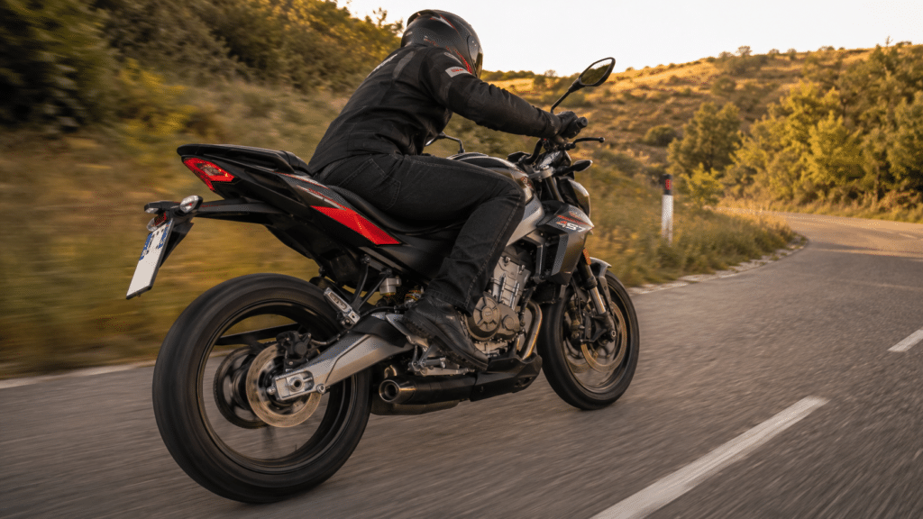 photorealistic, Aprilia Tuono 457 sporty naked A2 motorcycle in motion on a country road, sense of dynamic performance and Italian engineering, golden afternoon light, no rider face identifiable, three-quarter rear view emphasizing the sport exhaust and chassis, no watermark